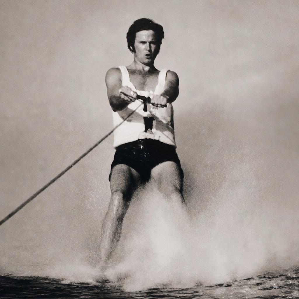 A younger Bill Perkins barefoot on the water in a white tank top